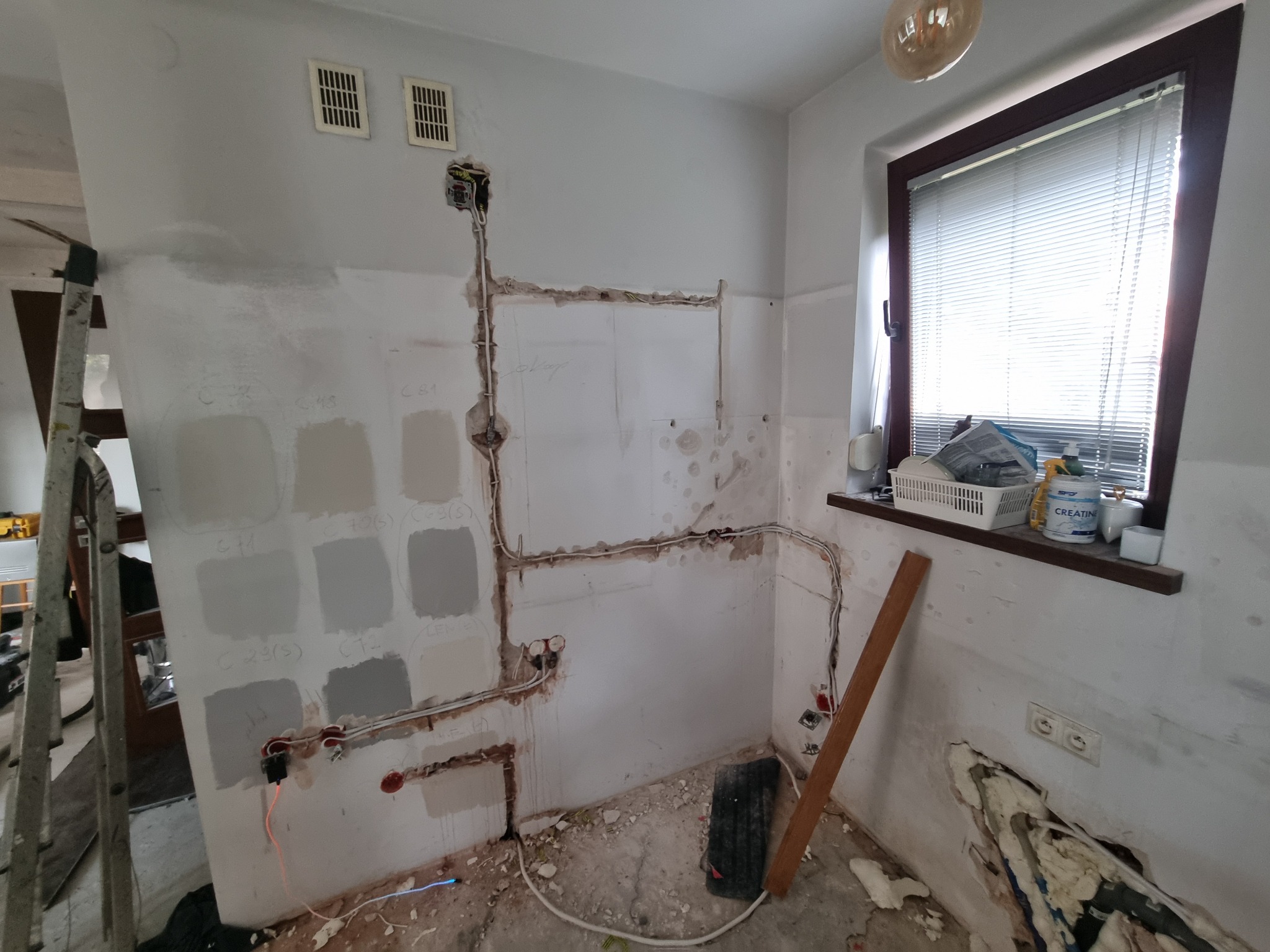 Instalacja elektryczna w trakcie remontu łazienki w Żyrardowie, widoczne kable poprowadzone po ścianach, przygotowane podłoże pod płytki oraz próbki kolorów farb na ścianie.