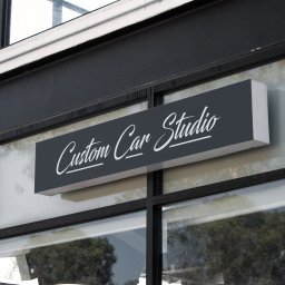 Krzysztof Baryła - Szyld reklamowy 'Custom Car Studio' z białym napisem na ciemnoszarym tle, zamontowany nad witryną sklepową z czarnymi ramami okiennymi.