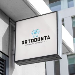 Krzysztof Baryła - Kwadratowy, podświetlany szyld reklamowy z logo gabinetu ortodontycznego, zamontowany na elewacji nowoczesnego budynku.