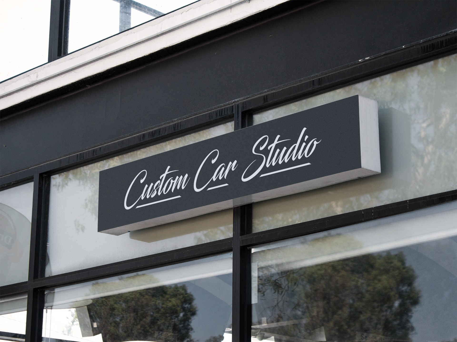Szyld reklamowy 'Custom Car Studio' z białym napisem na ciemnoszarym tle, zamontowany nad witryną sklepową z czarnymi ramami okiennymi.