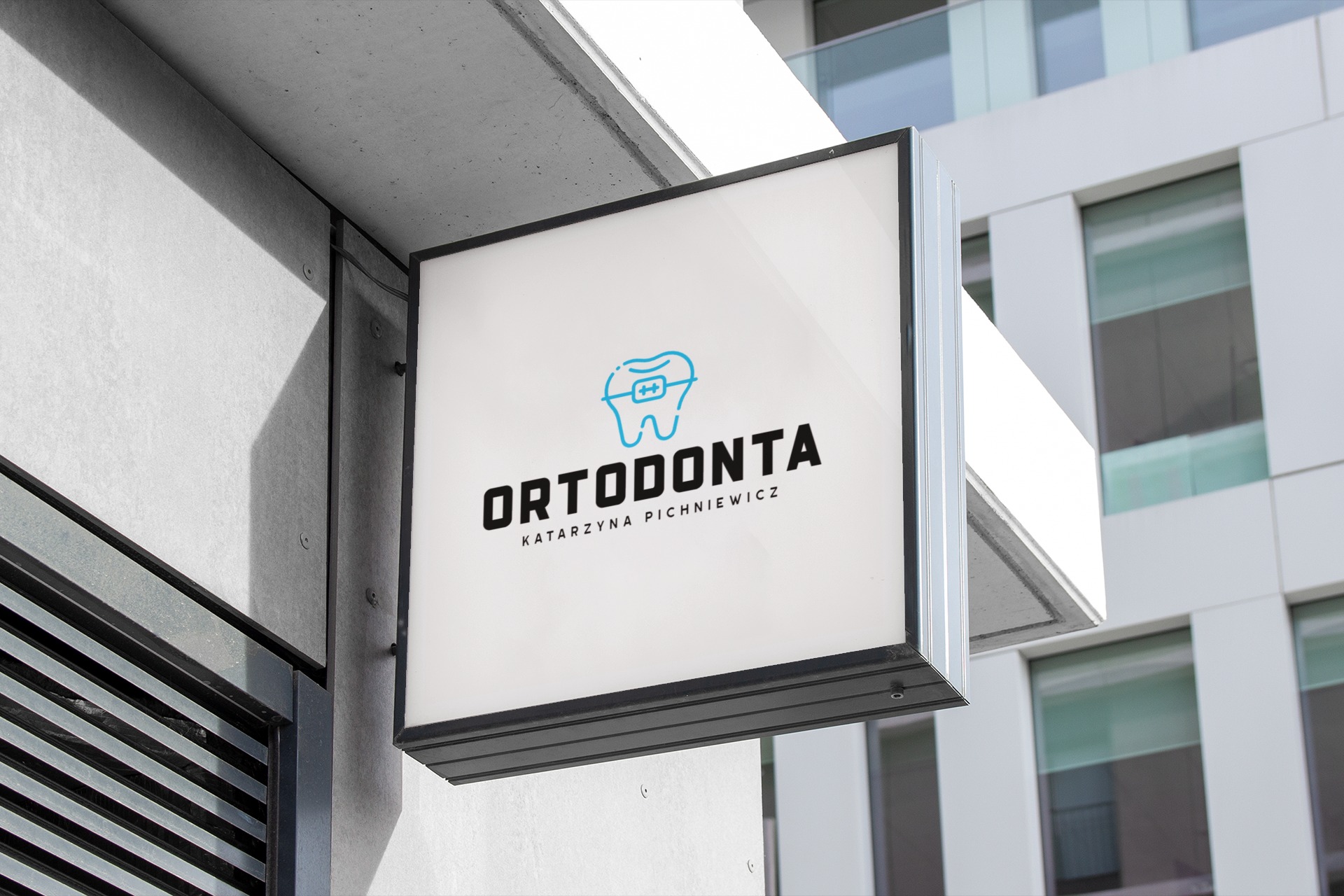 Kwadratowy, podświetlany szyld reklamowy z logo gabinetu ortodontycznego, zamontowany na elewacji nowoczesnego budynku.