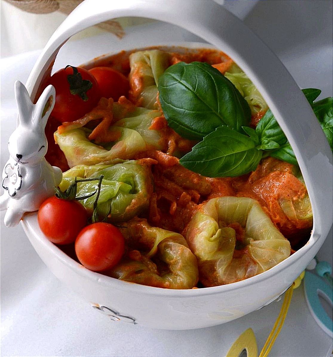 Gołąbki w sosie pomidorowym, podane w białym koszyczku z dekoracją w postaci ceramicznego zajączka i świeżej bazylii, uzupełnione pomidorkami koktajlowymi.