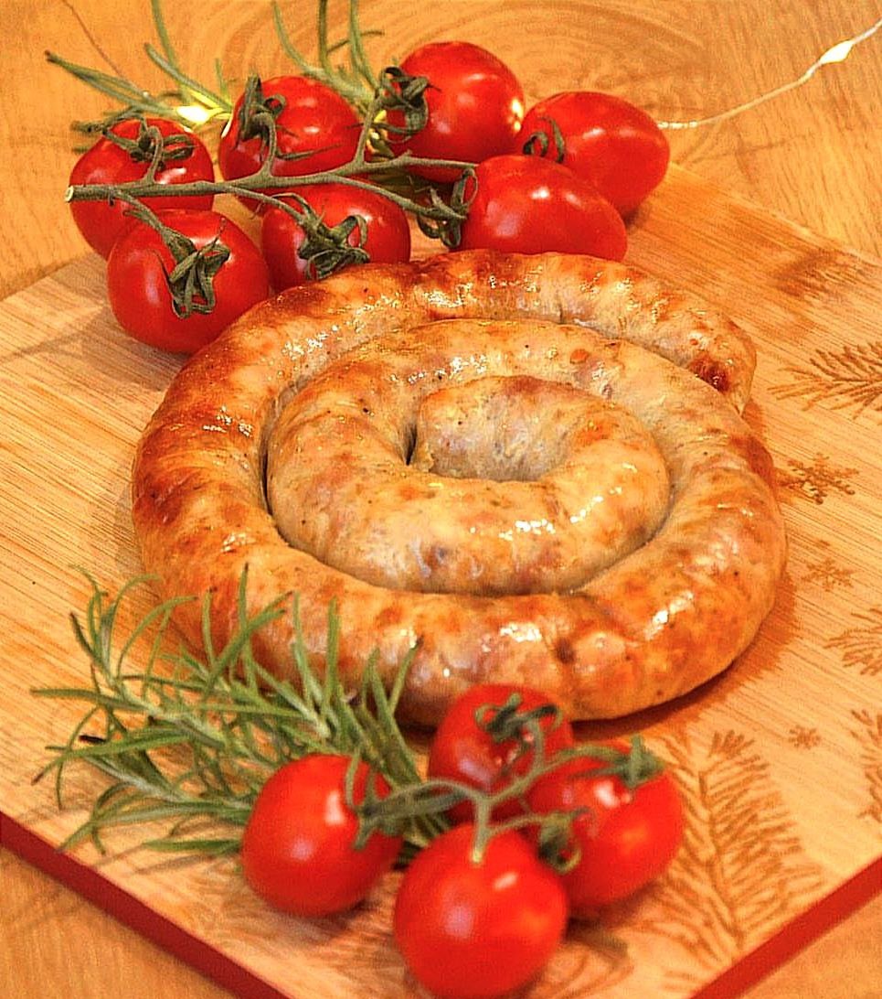Grillowana kiełbasa w kształcie spirali na drewnianej desce do krojenia, udekorowana gałązkami pomidorów cherry i rozmarynem, oświetlona ciepłym światłem.