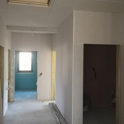 Robert Kalbarczyk - Korytarz w trakcie montażu płyt kartonowo-gipsowych, widoczne profile na podłodze, otwór okienny w suficie oraz instalacja elektryczna.