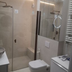 Robert Kalbarczyk - Nowoczesna łazienka z kabiną prysznicową typu walk-in, umywalką nablatową i toaletą podwieszaną. Lustro z oświetleniem LED i grzejnik drabinkowy.