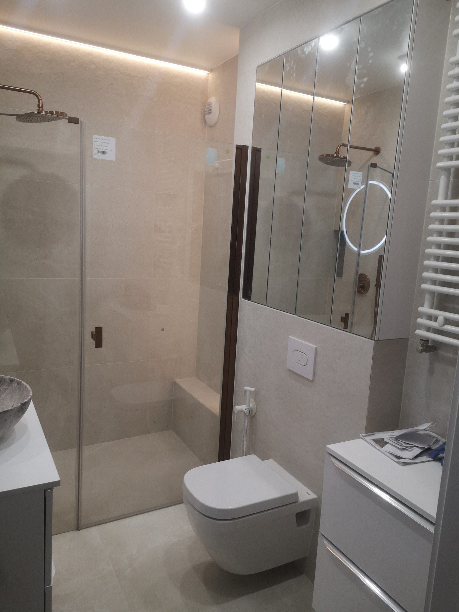 Nowoczesna łazienka z kabiną prysznicową typu walk-in, umywalką nablatową i toaletą podwieszaną. Lustro z oświetleniem LED i grzejnik drabinkowy.