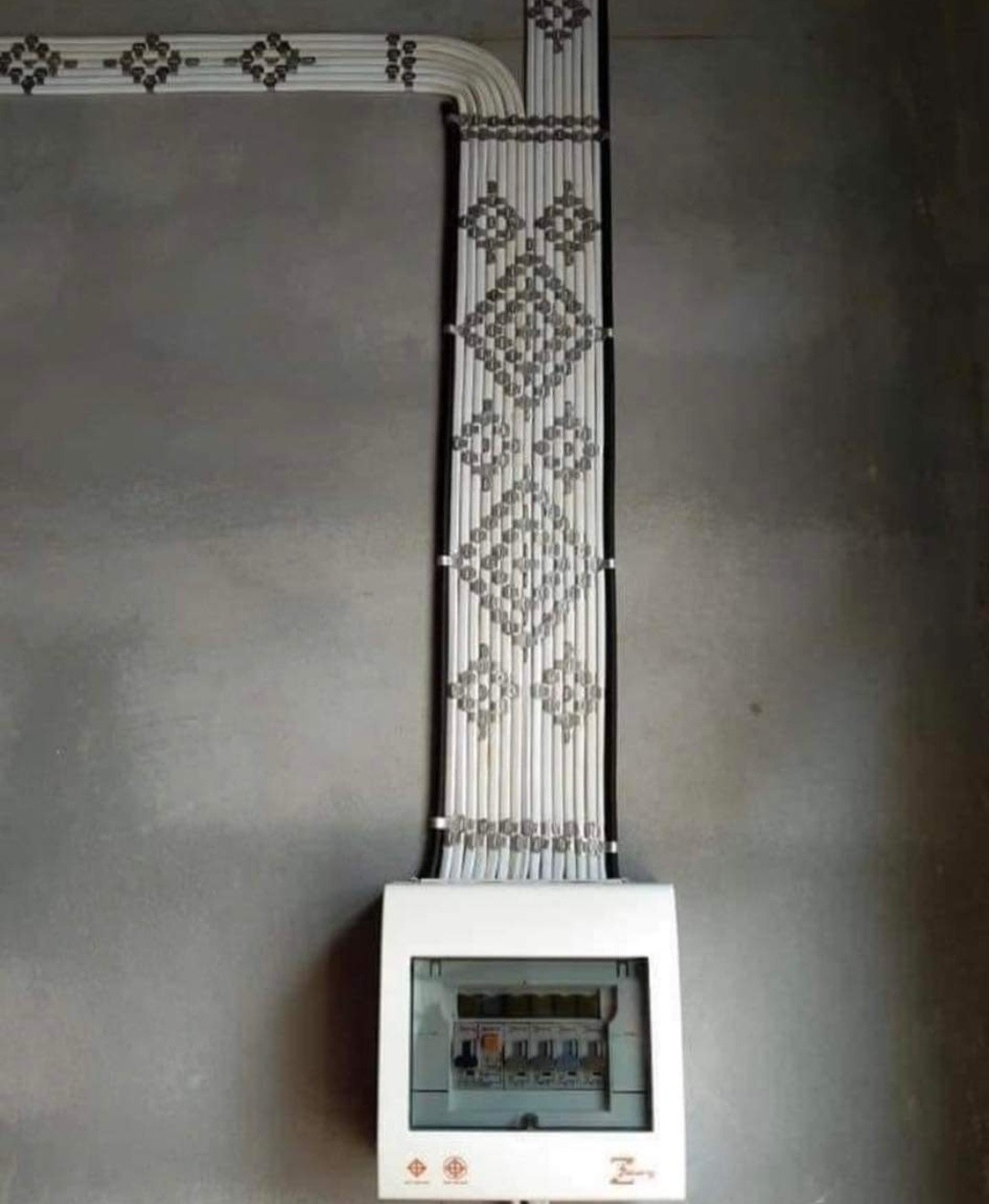 Elegancko ułożone kable elektryczne tworzące wzór na ścianie nad białą skrzynką rozdzielczą. Estetyczna instalacja w surowym wnętrzu.