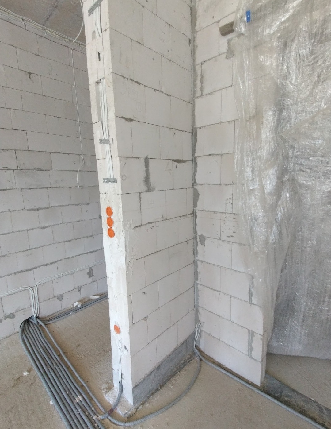 Surowy stan: instalacja elektryczna w ścianach z białych bloczków, kable w peszlach prowadzone po podłodze, otwory pod gniazdka zaznaczone na ścianie.