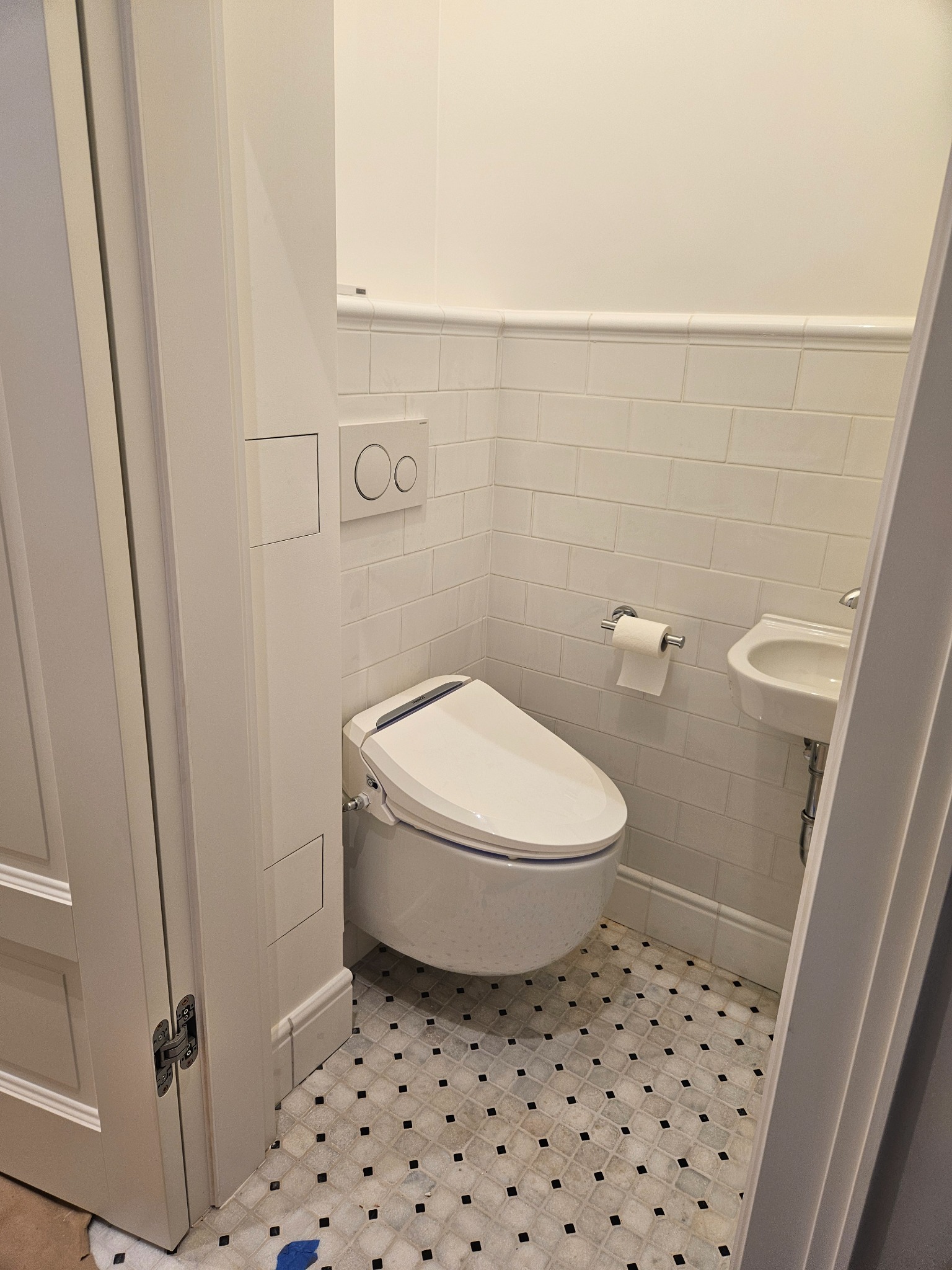 Biała toaleta myjąca z deską bidetową i podwieszana umywalka w małej, wykafelkowanej łazience z wzorzystą podłogą.