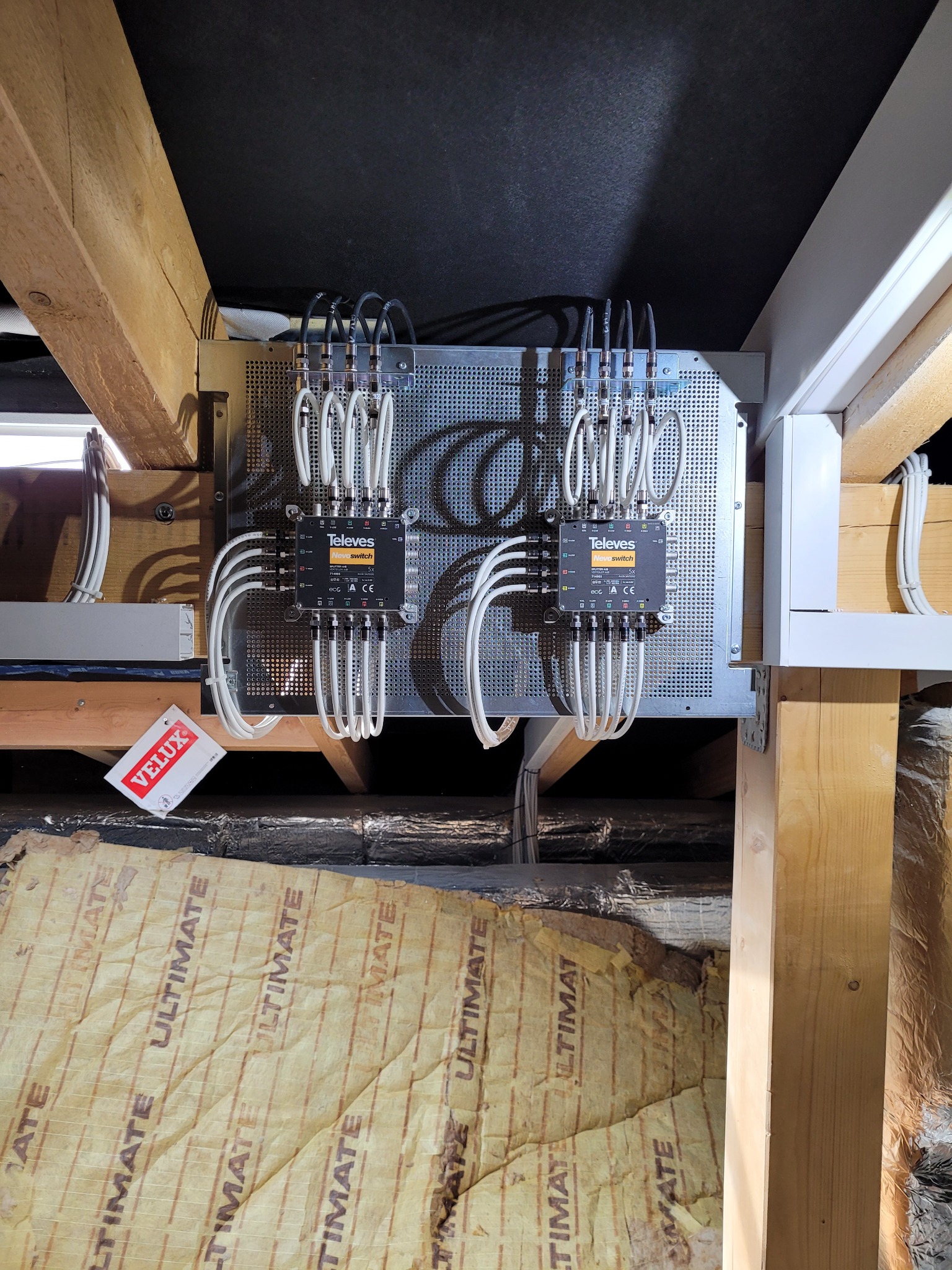 Dwa przełączniki Televes Novoswitch zamontowane na perforowanej płycie, z widocznymi kablami i elementami konstrukcji dachu. Widoczna etykieta Velux.