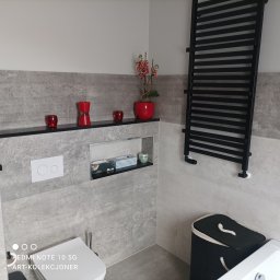 F.H.U. DARIUSZ RAKOWSKI - Nowoczesna łazienka z szarymi płytkami imitującymi kamień, podwieszana toaleta, czarny grzejnik drabinkowy, czerwone akcenty dekoracyjne i wnęka z akcesoriami.