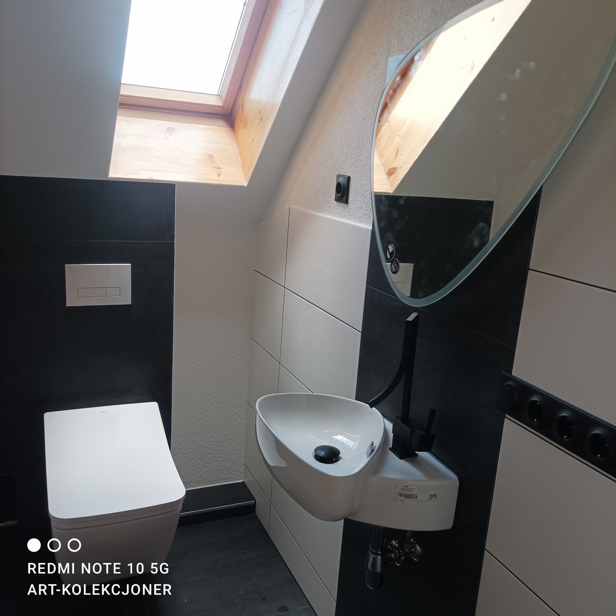 Nowoczesna łazienka na poddaszu z oknem dachowym, białą ceramiką i czarno-białymi płytkami, minimalistyczna armatura.