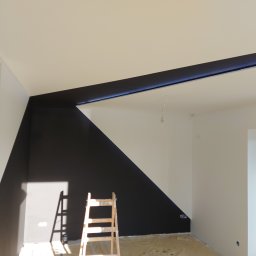 REM-ART ARTUR AFTYKA - Świeżo pomalowane wnętrze z geometrycznym podziałem kolorów na ścianie, widoczna drabina malarska i wystające przewody elektryczne.