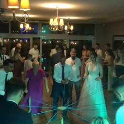 Gajewski Band - Goście weselni uczestniczący w zabawie z niebieskimi sznurkami, w tle para młoda i konferansjer z mikrofonem, oświetlenie sali z żyrandolami