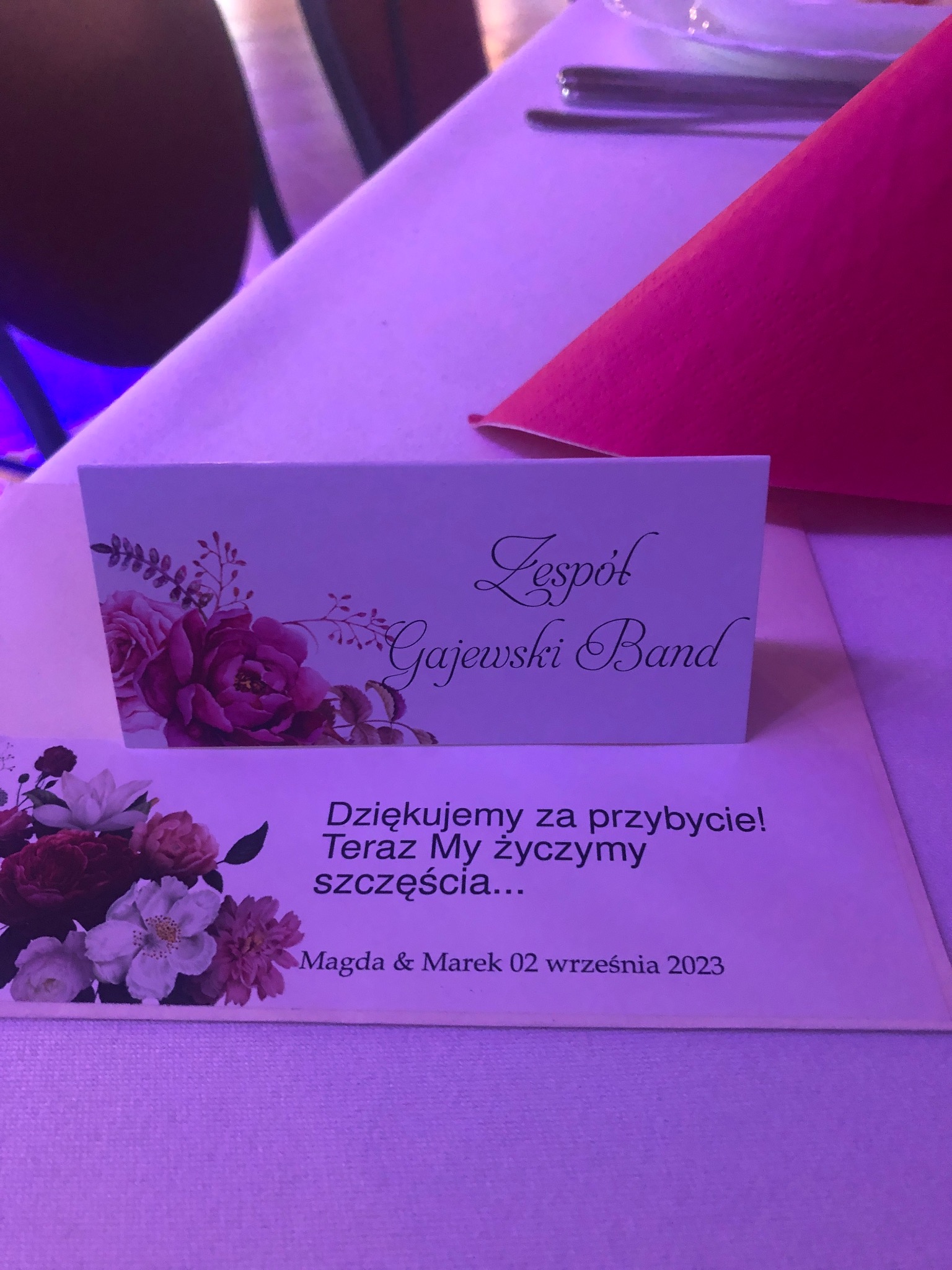 Winietka z nazwą zespołu muzycznego 'Gajewski Band' na stole weselnym, obok kartka z podziękowaniami dla gości weselnych od Magdy i Marka z datą 02 września 2023.