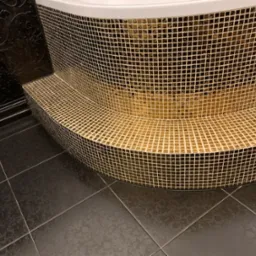 Mozaika w odcieniach złota i czerni zdobi obudowę wanny, kontrastując z ciemną, wzorzystą podłogą i ścianą, tworząc elegancki efekt wizualny.