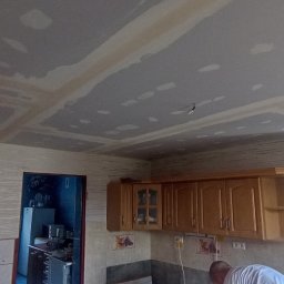Usługi budowlane Vladysław Kliatskyi - Sufit w kuchni po montażu płyt gipsowo-kartonowych, widoczne łączenia i szpachlowanie, elementy instalacji elektrycznej wystające z sufitu, częściowo widoczne umeblowanie kuchenne.