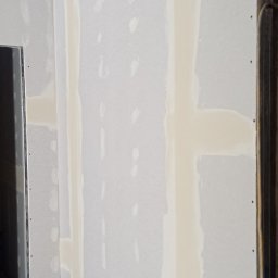 Usługi budowlane Vladysław Kliatskyi - Ściana z płyt kartonowo-gipsowych w trakcie szpachlowania, widoczne łączenia płyt i metalowa konstrukcja sufitu.