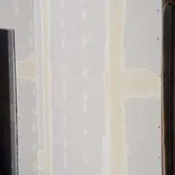 Ściana z płyt kartonowo-gipsowych w trakcie szpachlowania, widoczne łączenia płyt i metalowa konstrukcja sufitu.