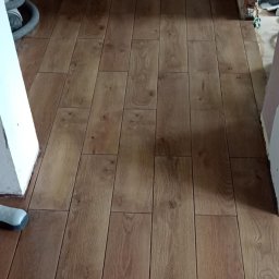 Usługi budowlane Vladysław Kliatskyi - Ułożone panele podłogowe imitujące drewno, widoczne worki z zaprawą w tle i niedokończone ściany.