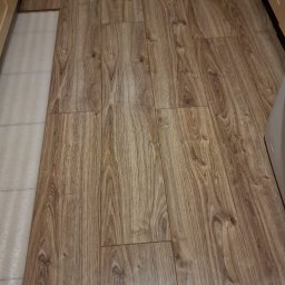 Usługi budowlane Vladysław Kliatskyi - Ułożone panele podłogowe o wzorze drewna, widoczne fragmenty białej podłogi i grzejnika.