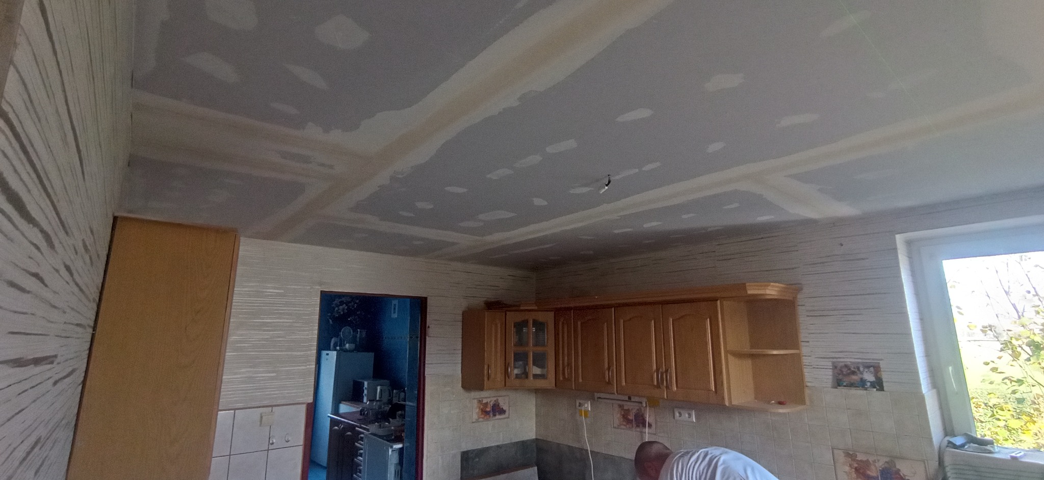 Sufit w kuchni po montażu płyt gipsowo-kartonowych, widoczne łączenia i szpachlowanie, elementy instalacji elektrycznej wystające z sufitu, częściowo widoczne umeblowanie kuchenne.