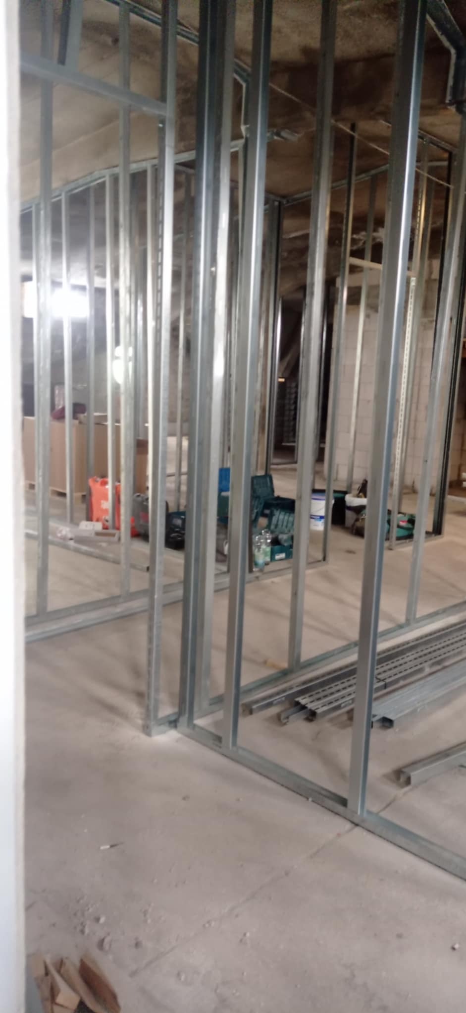 Konstrukcja szkieletowa ścian działowych z profili stalowych w trakcie montażu, widoczne narzędzia i materiały budowlane w tle.