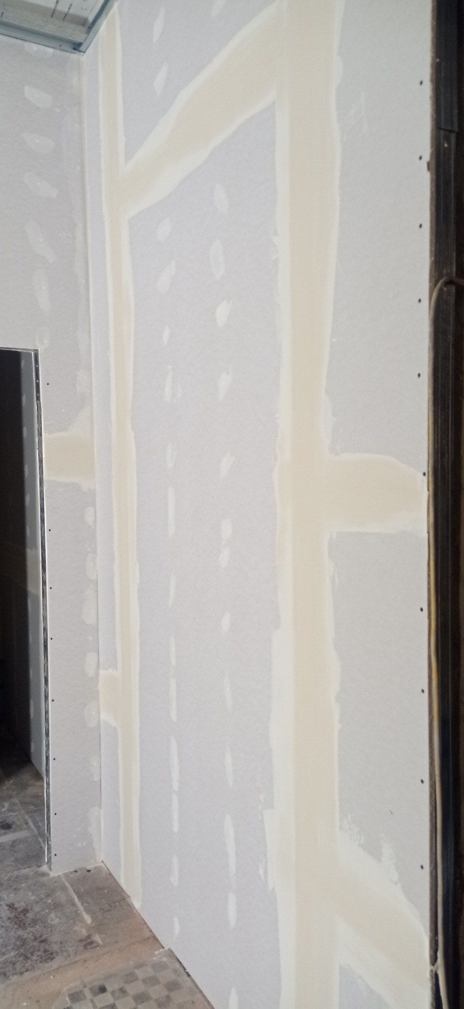 Ściana z płyt kartonowo-gipsowych w trakcie szpachlowania, widoczne łączenia płyt i metalowa konstrukcja sufitu.