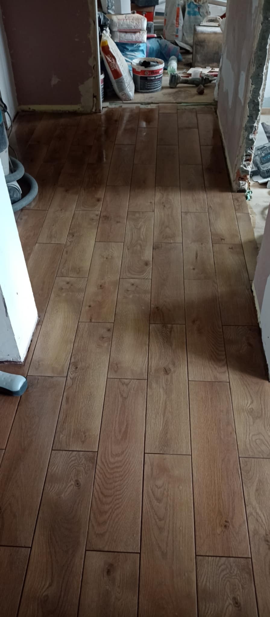 Ułożone panele podłogowe imitujące drewno, widoczne worki z zaprawą w tle i niedokończone ściany.