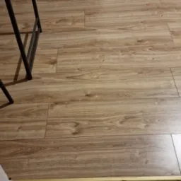 Ułożona podłoga z paneli imitujących drewno, widoczne fragmenty krzesła i futryny drzwi.