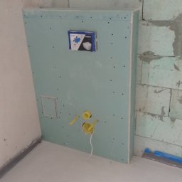 Usługi budowlane Wladysław Kliatskyi - Ścianka z płyty GK z instalacją podtynkową WC w trakcie montażu, widoczne żółte rury i otwór rewizyjny. Ściana z betonu komórkowego w tle.