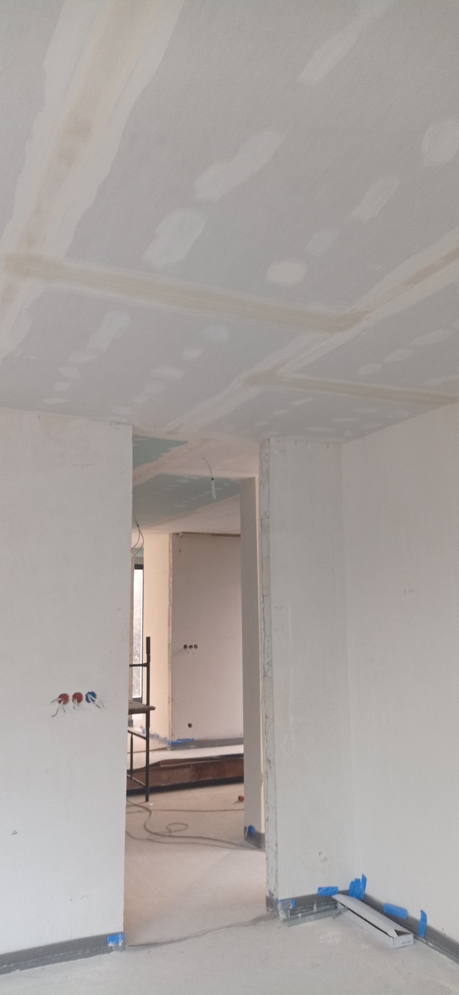 Wnętrze w trakcie prac wykończeniowych: sufit z płyt kartonowo-gipsowych, ściany przygotowane do malowania, widoczne instalacje elektryczne i fragment rusztowania.