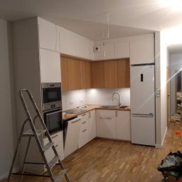 AleksandrijaBud Sp z OO - Ukończona kuchnia w stylu skandynawskim z białymi i drewnianymi szafkami, widok na zabudowane sprzęty AGD i drabina malarska w rogu.
