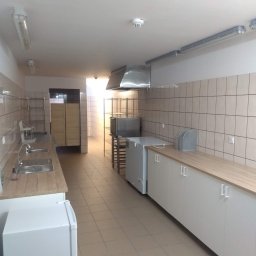 AleksandrijaBud Sp z OO - Wyposażone wnętrze kuchni przemysłowej z okapem, szafkami, blatem i lodówkami w jasnej tonacji.