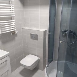 AleksandrijaBud Sp z OO - Nowoczesna łazienka z szarymi płytkami, wiszącą toaletą, kabiną prysznicową z ciemnymi szybami i białym grzejnikiem drabinkowym.