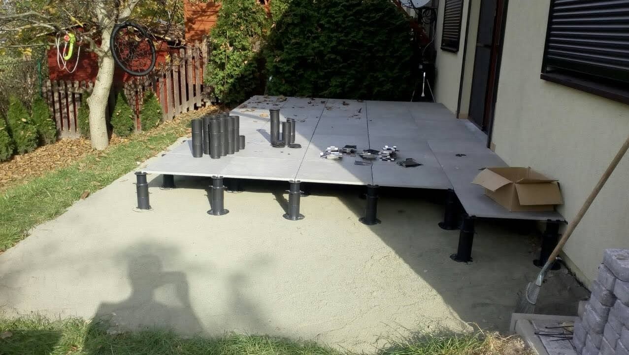 Montaż podestu tarasowego z regulowanymi wspornikami na piasku, widoczne elementy konstrukcyjne i narzędzia.