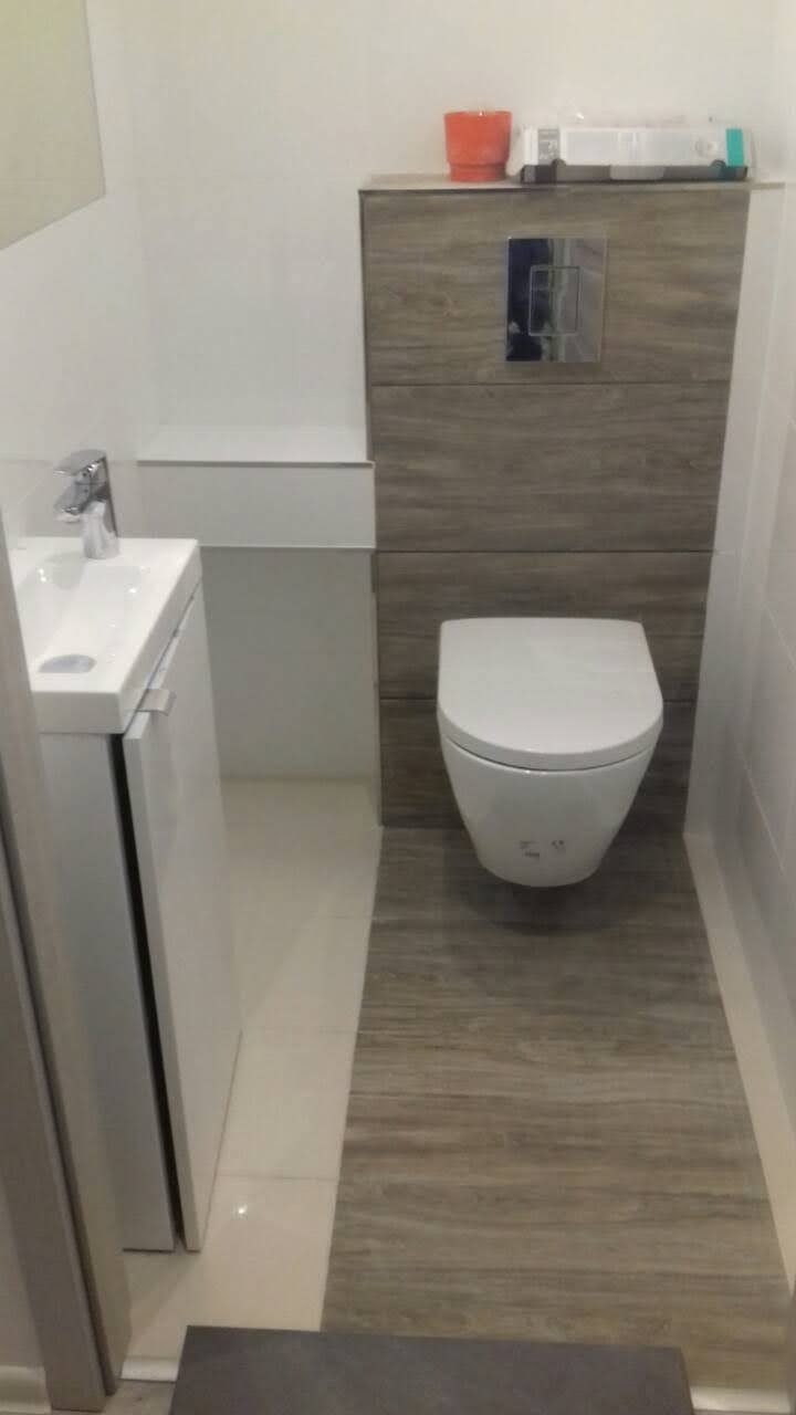 Nowoczesna łazienka z wiszącą toaletą, umywalką nablatową i płytkami imitującymi drewno na podłodze i obudowie stelaża podtynkowego.