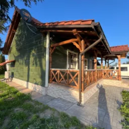 Zielony dom z drewnianą werandą, pomarańczową dachówką, widocznym systemem rynnowym i anteną satelitarną na dachu.