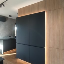 Concord Dmytro Hmyria - Nowoczesna zabudowa kuchenna z czarnymi frontami i drewnianymi panelami, oświetlona listwami LED, uzupełniona parkietem w jodełkę.