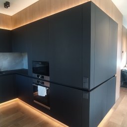 Concord Dmytro Hmyria - Nowoczesna kuchnia z czarnymi matowymi frontami, podświetleniem LED pod szafkami i na górze, drewniana podłoga i okładzina ścienna, minimalistyczne oświetlenie punktowe.