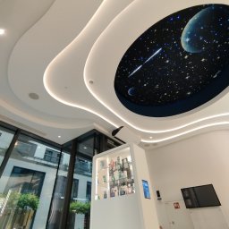 Concord Dmytro Hmyria - Nowoczesne wnętrze biura z falistym sufitem podwieszanym i oświetleniem LED, w centralnej części sufitu dekoracja imitująca kosmos z planetami i gwiazdami, przeszklona ściana z widokiem na zieleń.