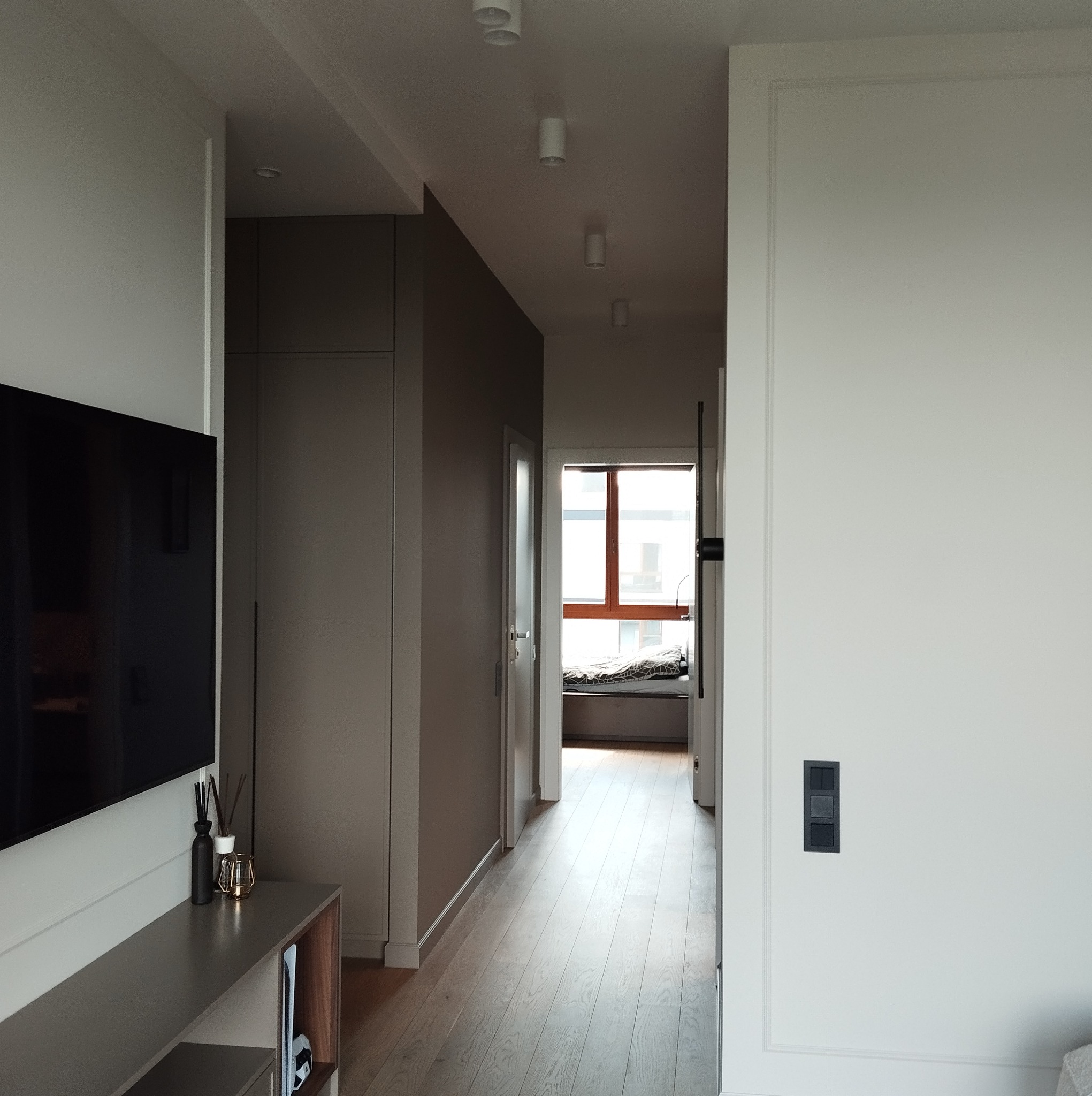 Wnętrze mieszkania z widokiem na korytarz i okno z miejscem do siedzenia, minimalistyczny design, drewniana podłoga, szafa w zabudowie w kolorze taupe, dekoracje na szafce RTV.