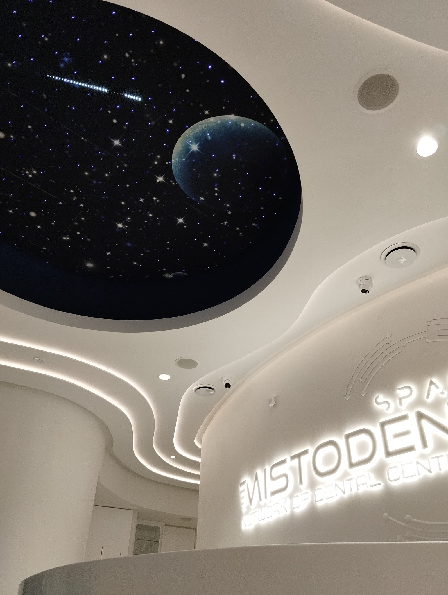 Recepcja w biurze z podświetlanym logo 'MISTODENT' i sufitem z motywem kosmosu: gwiazdy, księżyc i kometa