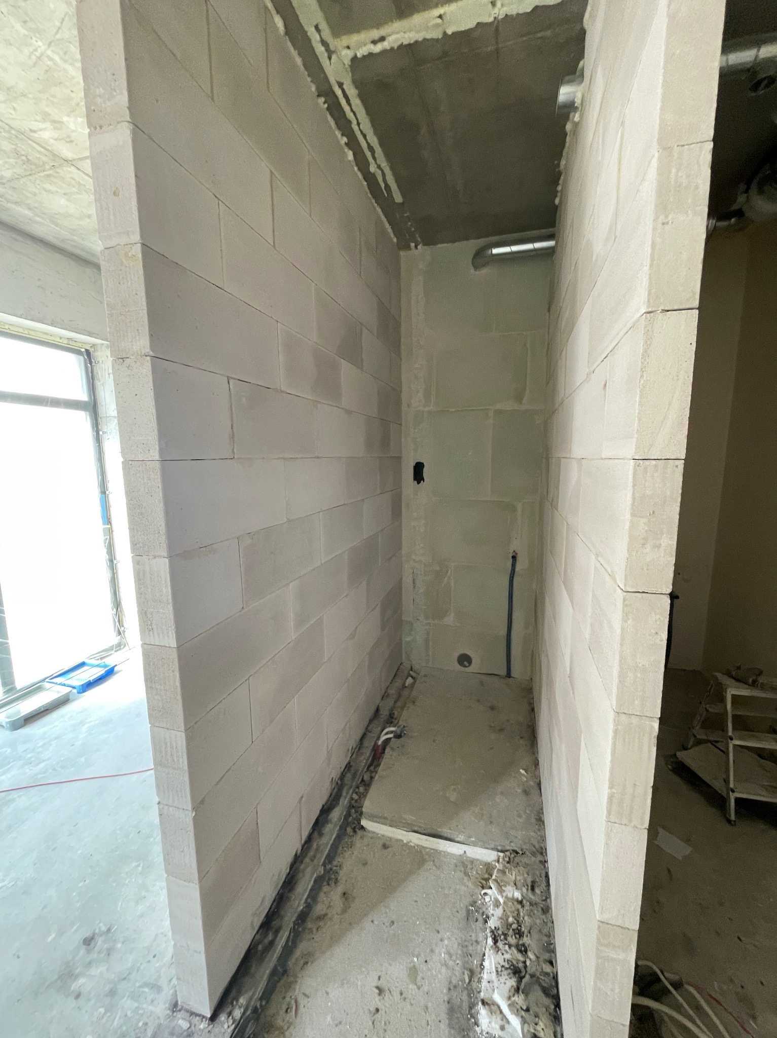 Wnętrze w trakcie budowy: ściany z bloczków z betonu komórkowego, widoczne instalacje, surowy betonowy strop, okno z widokiem na zewnątrz, przygotowane podłoże pod posadzkę.