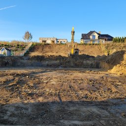 MDM COUNSTRUCTION SPÓŁKA Z OGRANICZONĄ ODPOWIEDZIALNOŚCIĄ - Wykop pod budowę domu jednorodzinnego w słoneczny dzień. Widoczny żółty sprzęt budowlany i ziemia. W tle zabudowa domów i błękitne niebo.