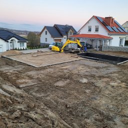 MDM COUNSTRUCTION SPÓŁKA Z OGRANICZONĄ ODPOWIEDZIALNOŚCIĄ - Żółta mini koparka przy budowie fundamentów pod basen na terenie budowy z domami w tle. Widoczne wykopane fundamenty i pracownicy.