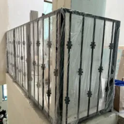 Nowa balustrada metalowa z dekoracyjnymi elementami, zabezpieczona folią ochronną na schodach w trakcie prac wykończeniowych.