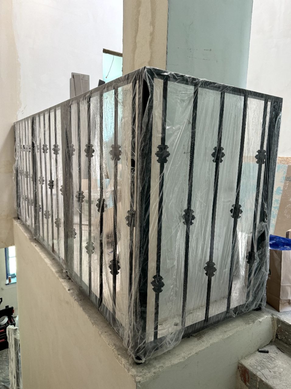 Nowa balustrada metalowa z dekoracyjnymi elementami, zabezpieczona folią ochronną na schodach w trakcie prac wykończeniowych.