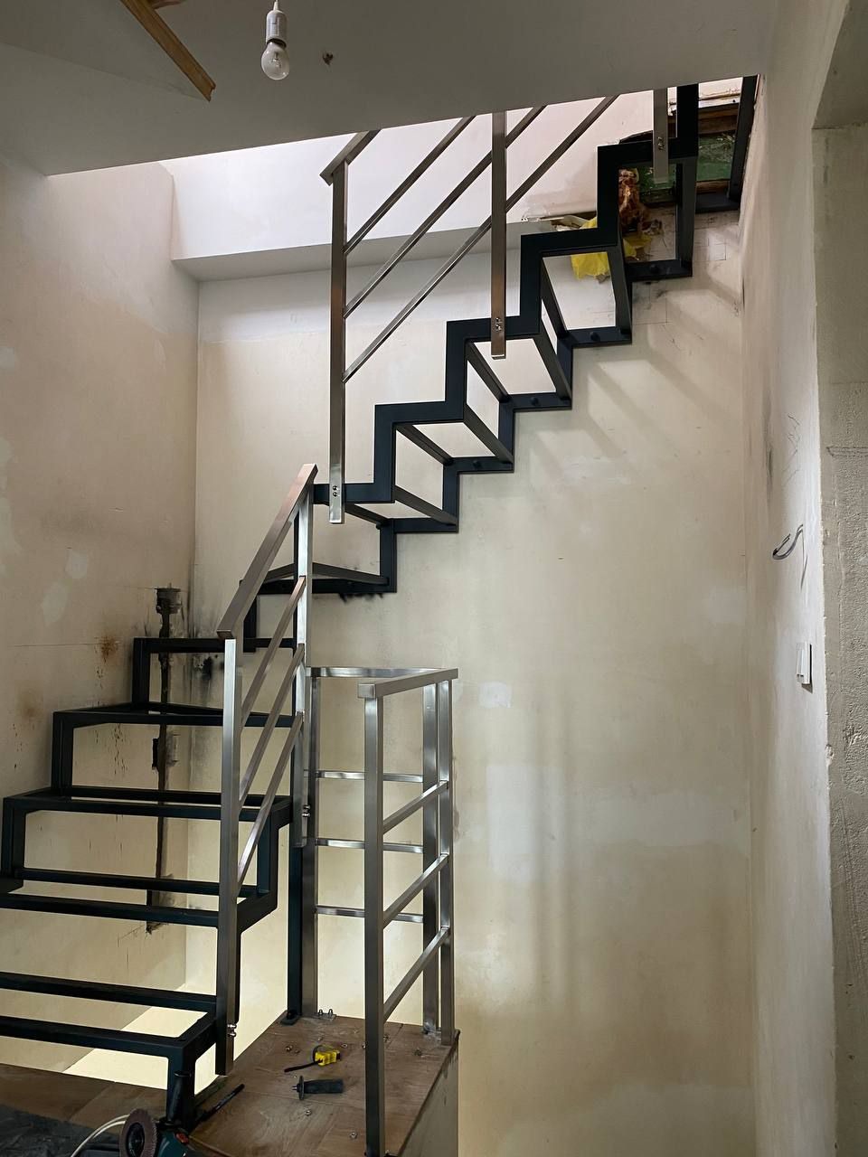 Wewnętrzne schody metalowe w trakcie montażu, z surową, nieotynkowaną ścianą w tle, widoczne narzędzia pracy i elementy konstrukcyjne.