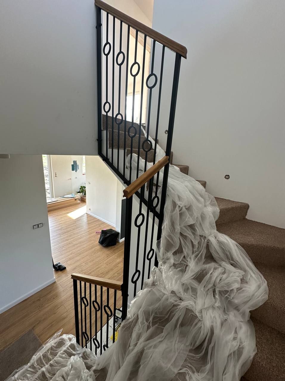 Klatka schodowa z nową, czarną balustradą z drewnianym poręczą, częściowo zabezpieczona folią ochronną podczas remontu, widok z góry na drewnianą podłogę na dole.